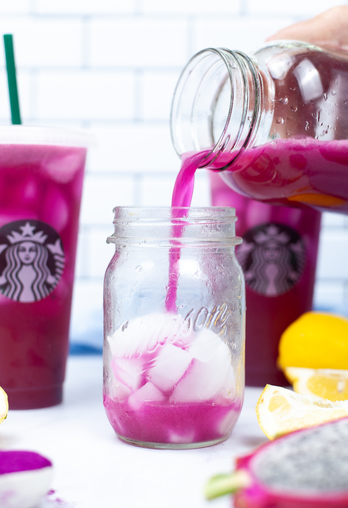 Blended drink with dragon fruit being poured in a mason jar glass filled with ice. 