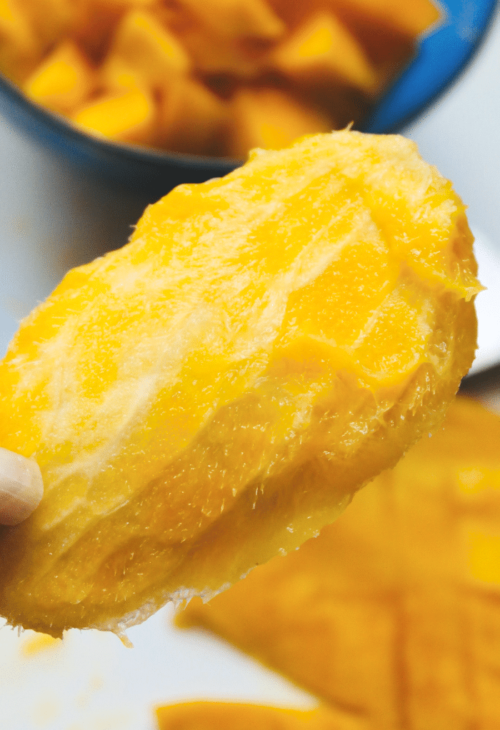 Fingers holding the pit of a mango after being sliced. 