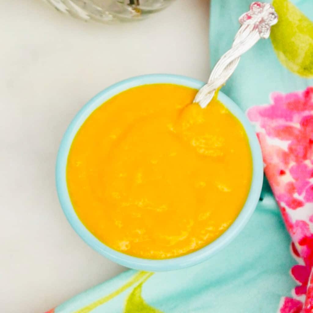 Mango pureed and in a teal small serving bowl with a silver spoon.