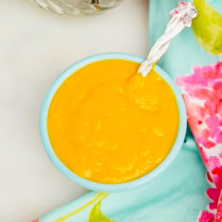 Mango pureed and in a teal small serving bowl with a silver spoon.