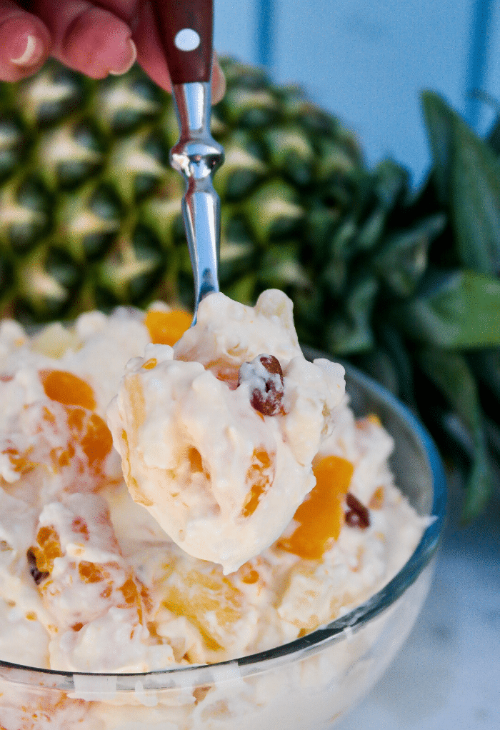 A spoonful of orange jello salad with mandarin oranges and pineapple. 