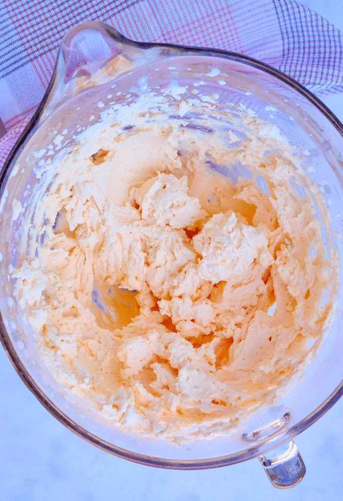 Whipped cream with orange jello in an clear bowl.