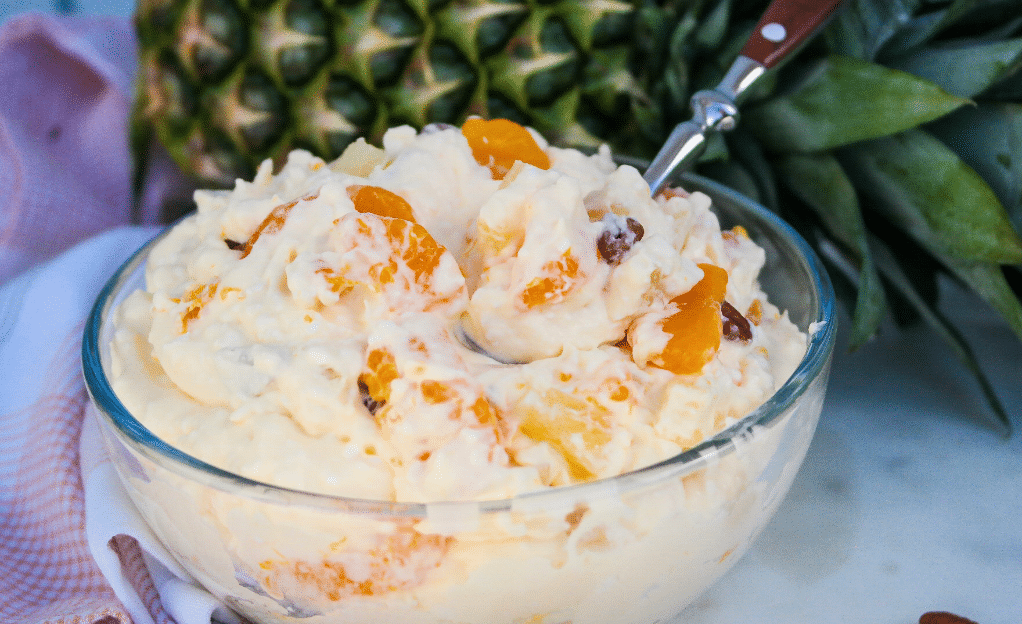 A fluffy whipped cream fruit salad with mandarin oranges and cottage cheese in a clear bowl.