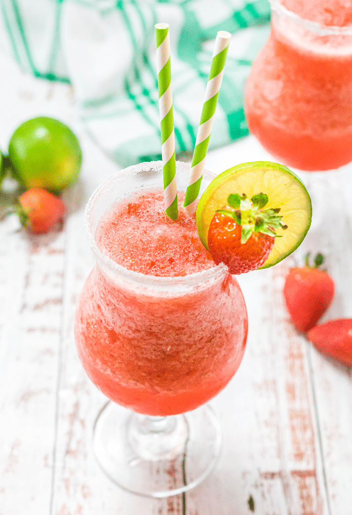 Virgin strawberry daiquiri in clear glasses topped with slice of lime and fresh strawberry.