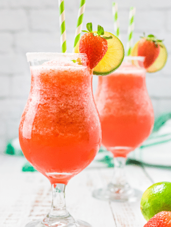 Two hurricane glasses with strawberry daiquiri topped with fresh fruit.