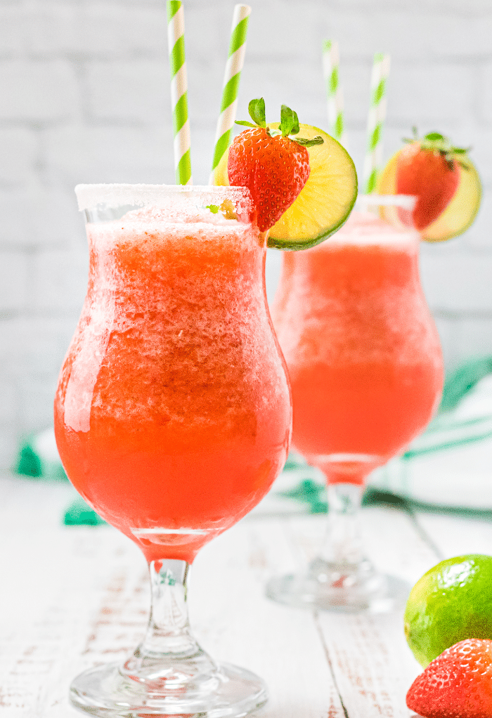 Two hurricane glasses with strawberry daiquiri topped with fresh fruit.