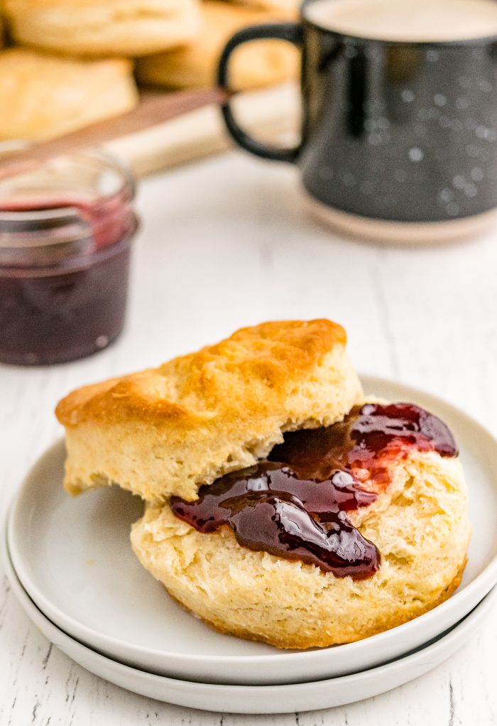 Homemade biscuit split in have and topped with jam on a white plate. 