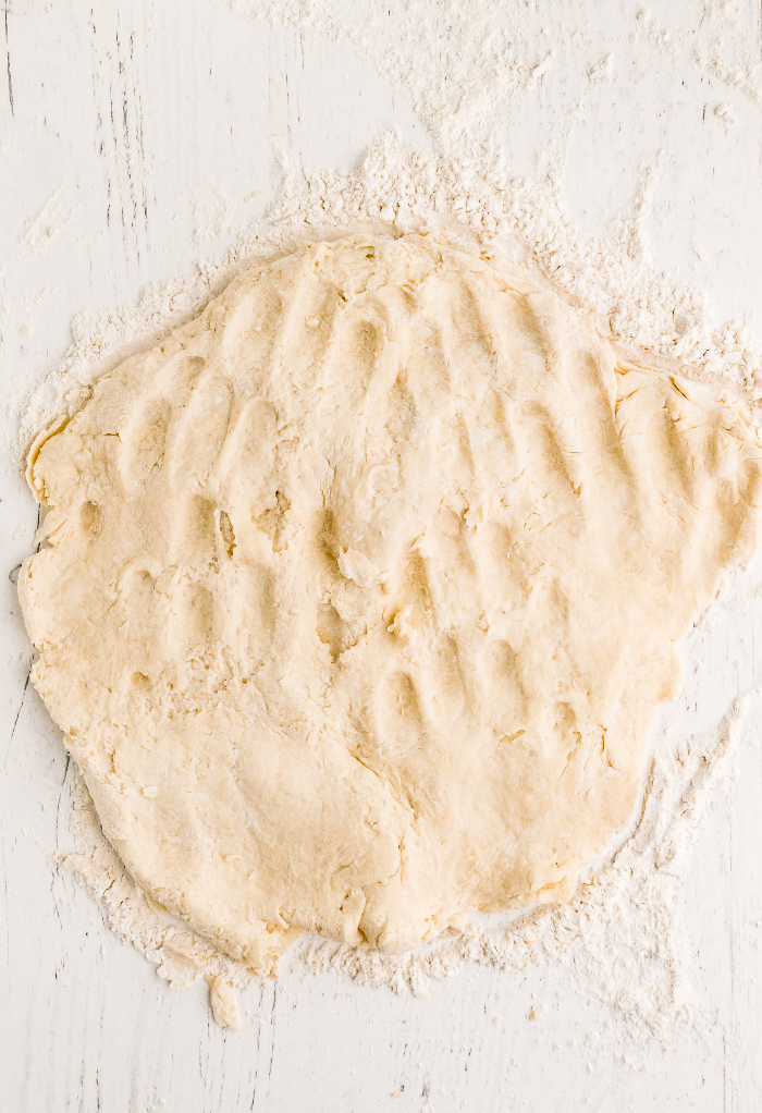 Biscuit dough patted with hands ready to cut into biscuits to bake. 