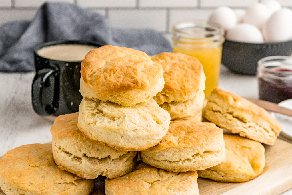 Buttermilk biscuits piled on each other with coffee and jam in the background. 