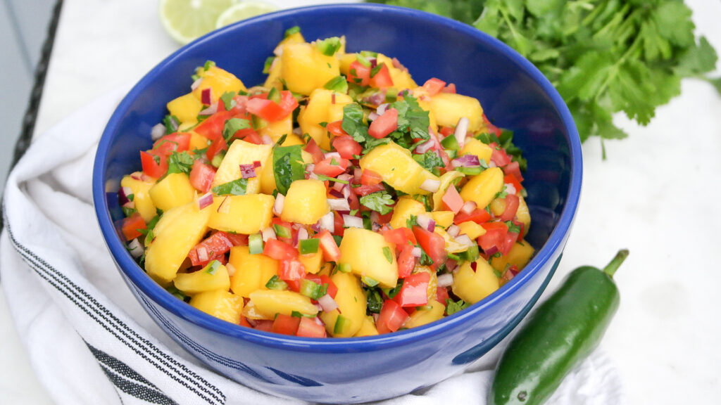 Blue bowl with mango pico de gallo ready to enjoy with a jalapeno on the side. 