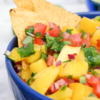 Homemade mango pico de gallo in a blue serving bowl with tortilla chips on the side.