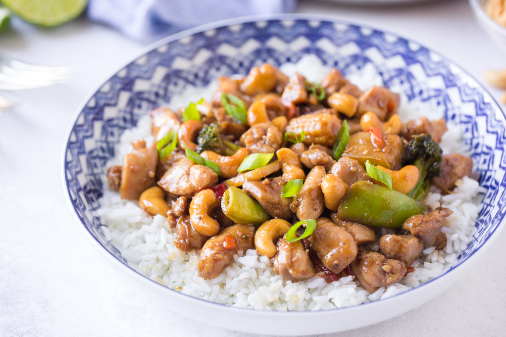 Teriyaki chicken with cashews in a white bowl with a blue rim. 