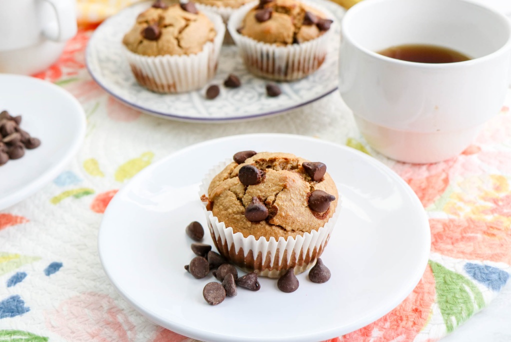 Muffin on a white plate with a white coffee cup on the side. 