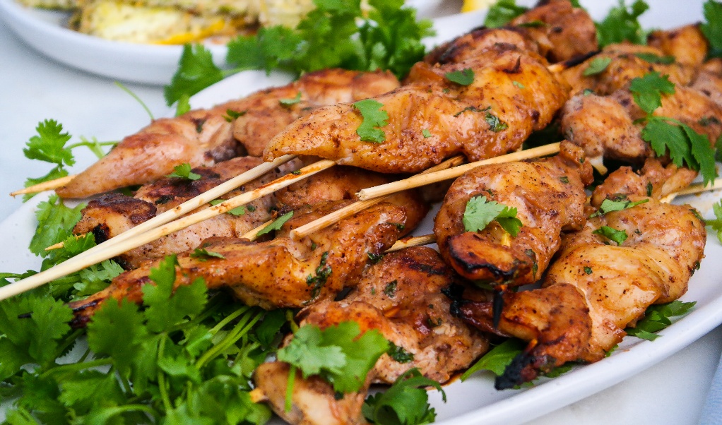 A white platter with chicken skewers.