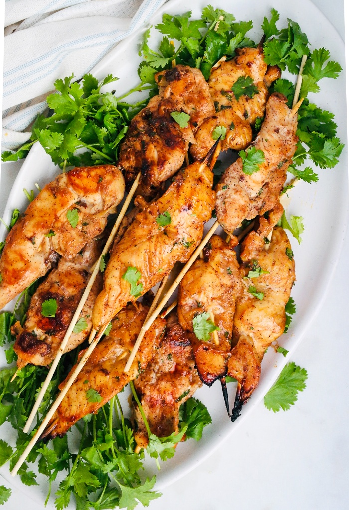 Top view of cooked chicken skewers on a white platter. 