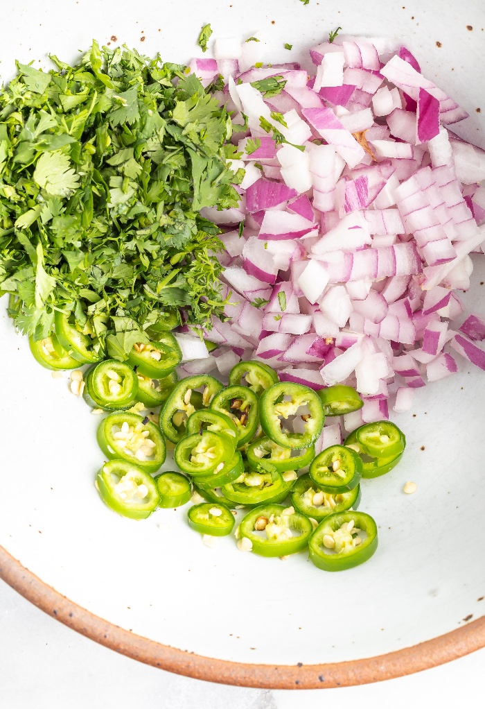 Ingredients to make pineapple salsa in a white mixing bowl.