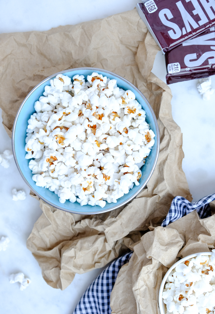 Overhead view of a bowl of popped popcorn with some chocolate bars on the side. 