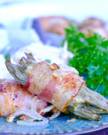 Fresh green beans wrapped in bacon on a teal plate.