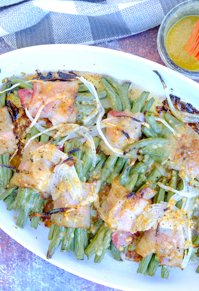 Fresh green beans wrapped in slices of bacon on a serving dish.