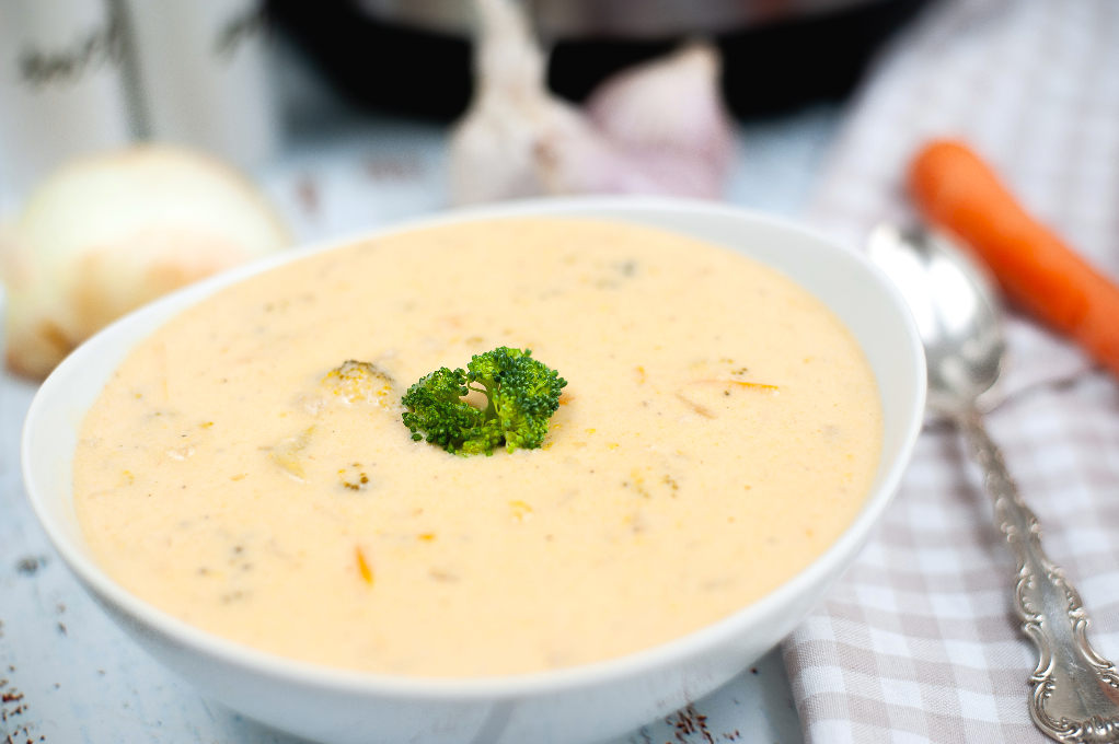 A bowl with cheese and broccoli soup and a spoon on the side.