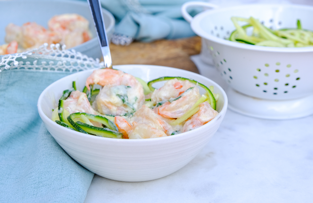 A white bowl with shrimp in a creamy Alfredo sauce.