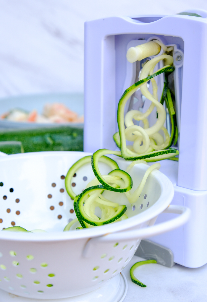 Hand held spiralizer with zucchini noodles in a white colander.  