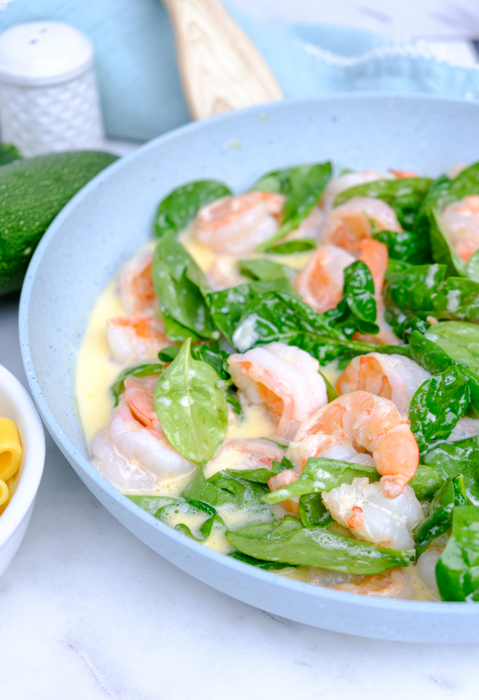 Shrimp and spinach in a skillet with Alfredo sauce.