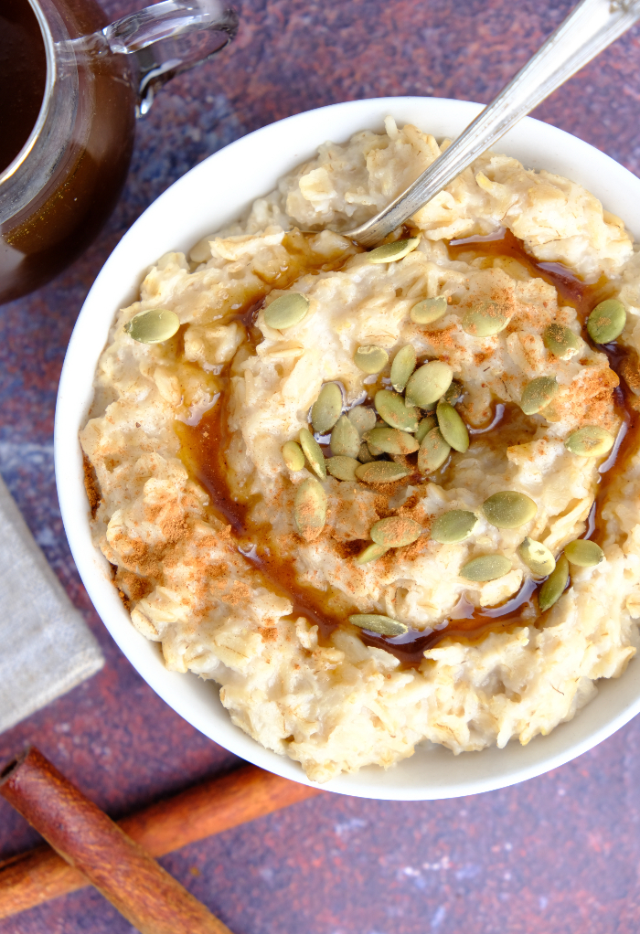 Top view of a white bowl with oatmeal topped with pumpkin seeds and syrup.