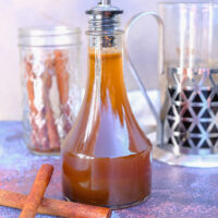 A clear glass container with a pour spout filled with homemade pumpkin spice syrup.