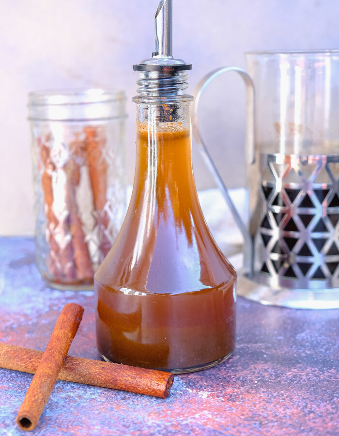 A clear glass container with a pour spout filled with homemade pumpkin spice syrup.