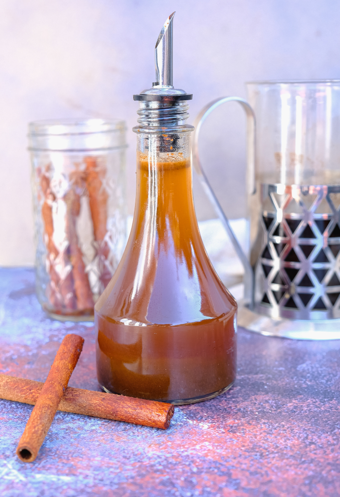 A clear glass container with a pour spout filled with homemade pumpkin spice syrup.
