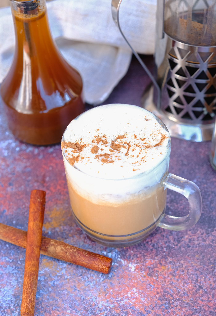 A hot mug of coffee with cinnamon sticks on the side