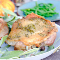Baked turkey thighs on a white serving plate with fresh sage.