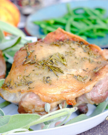 Baked turkey thighs on a white serving plate with fresh sage.
