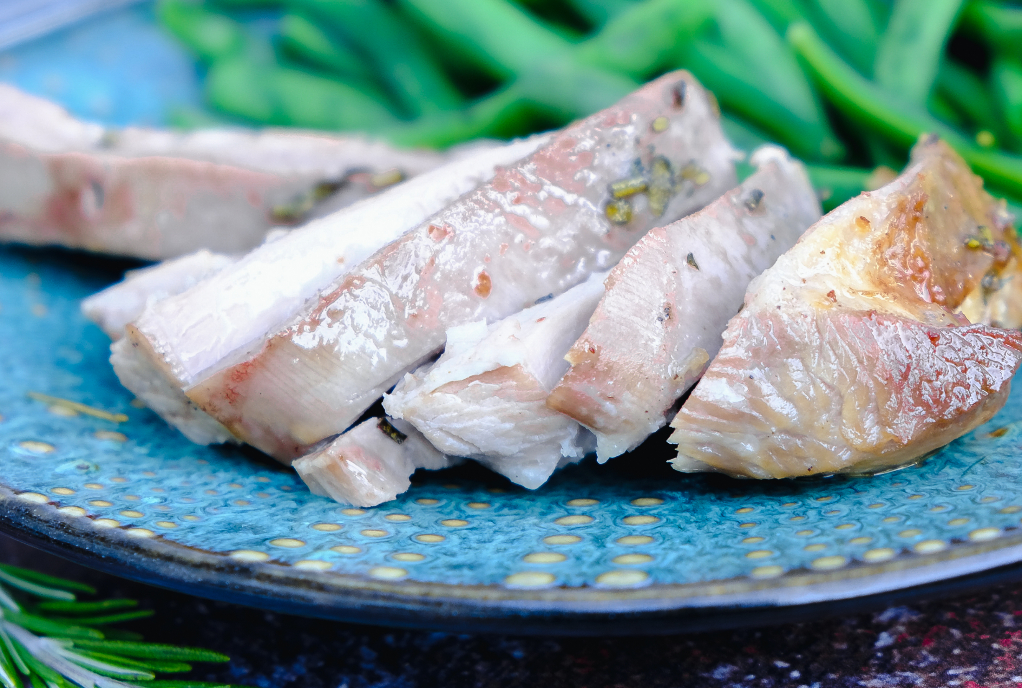 Sliced turkey thighs on a green-blue plate with green beans in the background. 