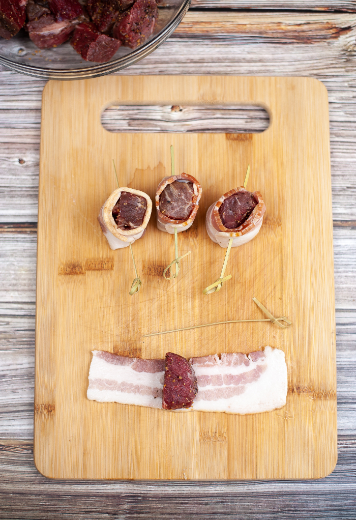 Top view of wrapping steak bites with bacon before cooking.