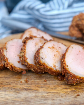 Air fryer pork tenderloin on a brown cutting board.
