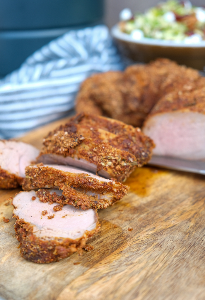 Sliced pork tenderloin on a brown cutting board. 