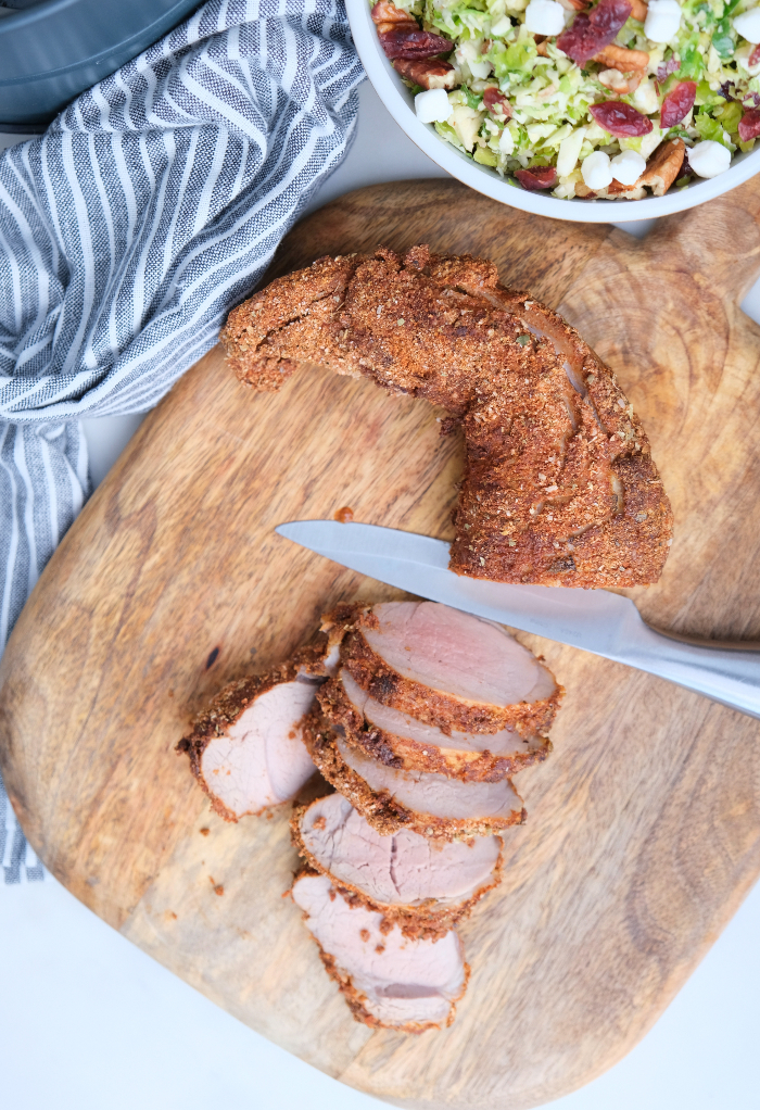 Top view of sliced pork tenderloin on a brown cutting board cooked in an air fryer.