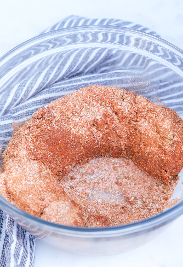 Pork tenderloin with spices in a clear mixing bowl.