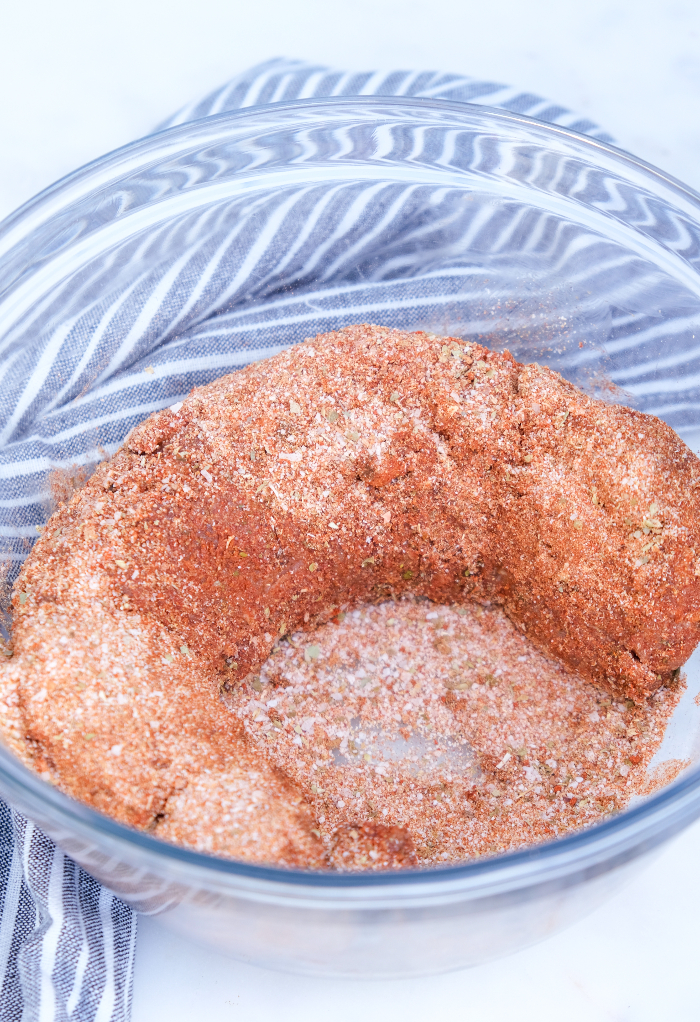 Pork tenderloin with spices in a clear mixing bowl. 