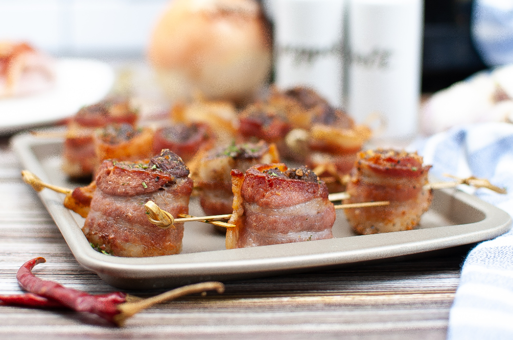 A baking sheet with steak covered bacon.