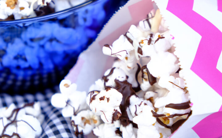 Popcorn drizzled in chocolate in small colorful paper bags ready to eat.