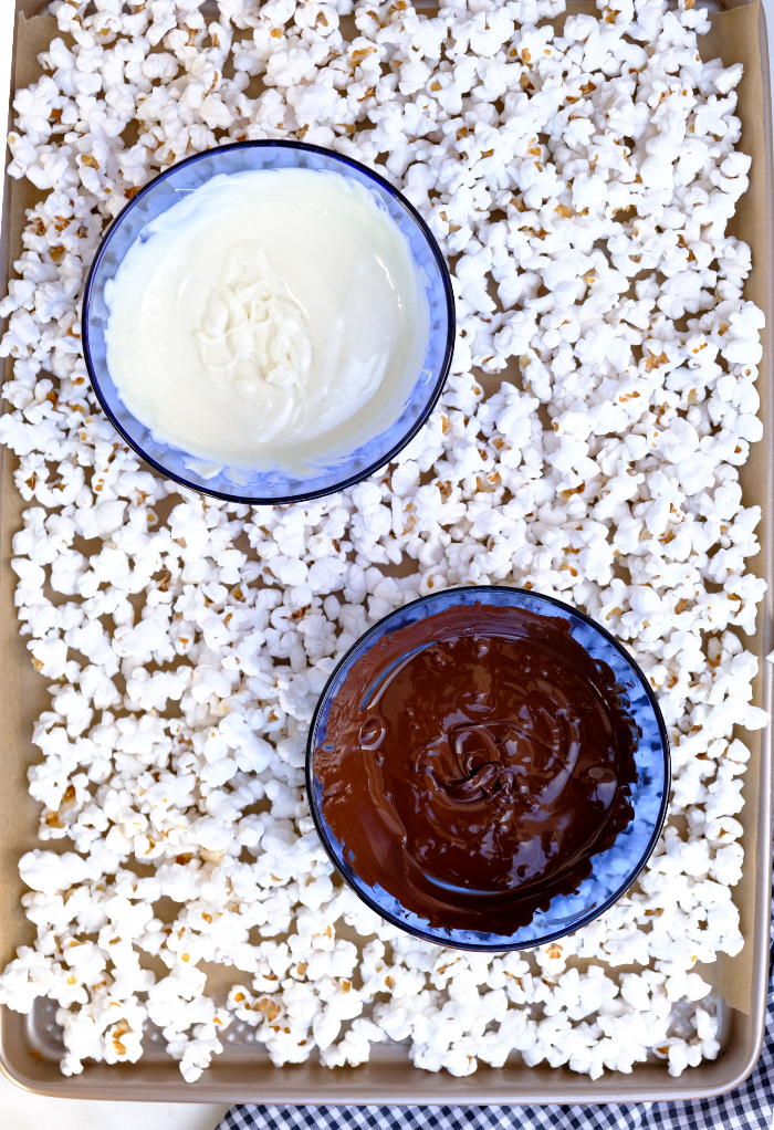 Melted white and dark chocolate with fresh popcorn on a baking sheet.