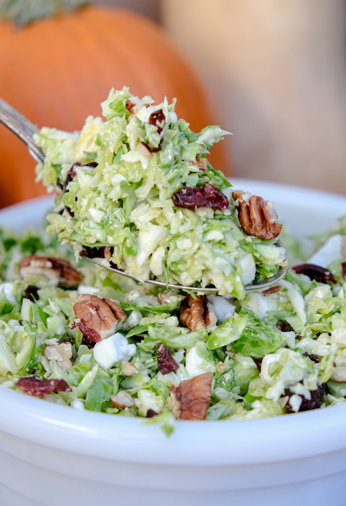 Brussel sprout salad in a white bowl with a spoon scooping up a serving.