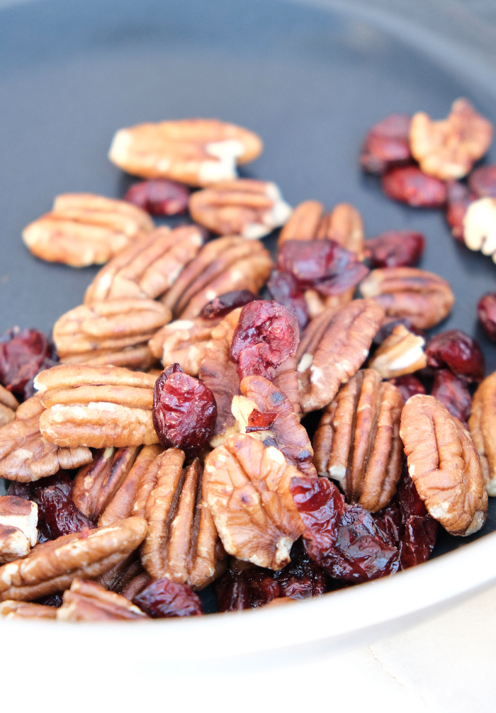 Toasting pecans in a skillet with dried cranberries.