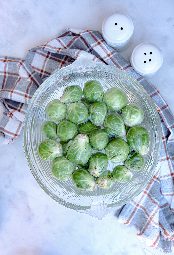 A clear bowl filled with water and Brussel sprouts.