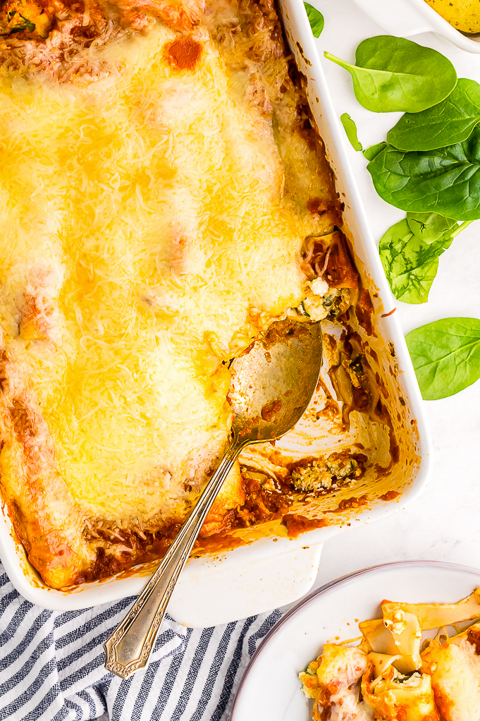 Spinach manicotti in a casserole dish and a plate on the side with manicotti.