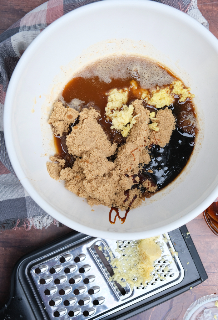 Sugar and molasses added to spice mix in white mixing bowl for gingersnap cookies.