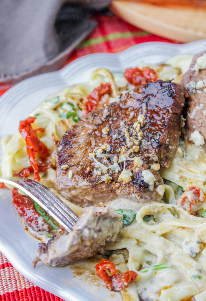 Sliced steak topped with balsamic and gorgonzola cheese over pasta.